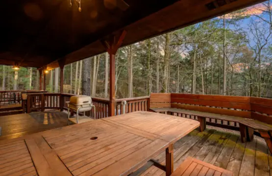 Spacious covered deck with cornhole, dining table, and stunning forest views perfect for relaxing outdoors.