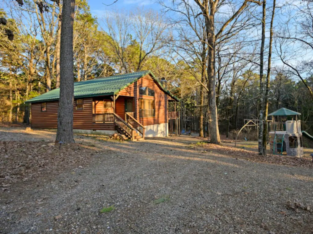 Cozy log cabin nestled in the woods with a covered porch and plenty of mature trees for that peaceful forest retreat vibe.