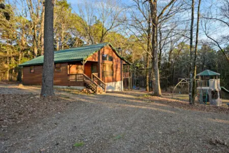 Cozy log cabin nestled in the woods with a covered porch and plenty of mature trees for that peaceful forest retreat vibe.
