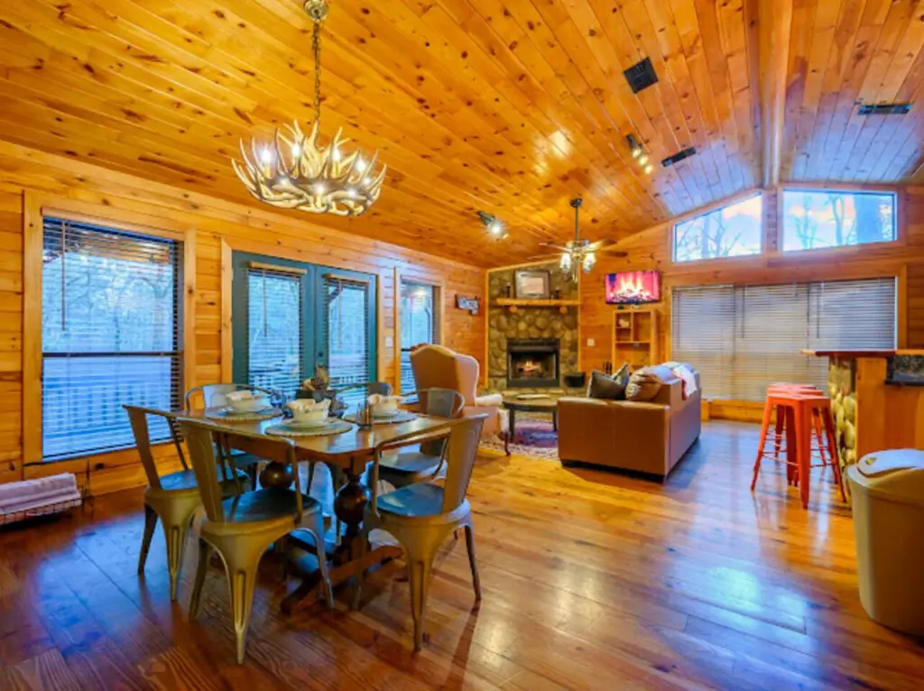 This spacious log cabin living area features soaring wood ceilings, a fireplace, and floor-to-ceiling windows with stunning views.