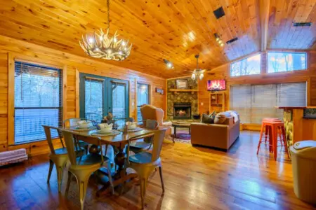 This spacious log cabin living area features soaring wood ceilings, a fireplace, and floor-to-ceiling windows with stunning views.