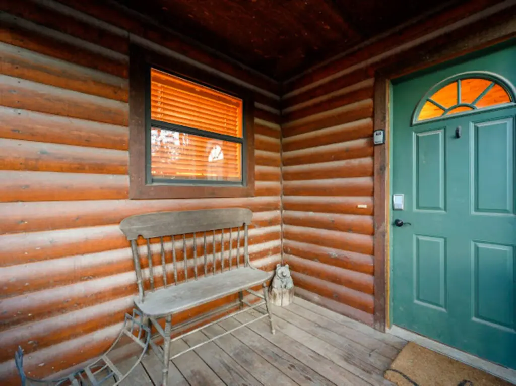 Cozy log cabin interior with a classic wooden bench, green entry door, and warm wood-beamed ceilings.