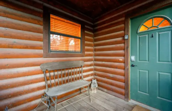 Cozy log cabin interior with a classic wooden bench, green entry door, and warm wood-beamed ceilings.
