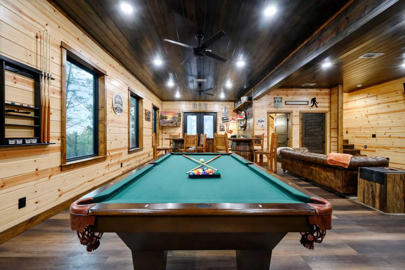 This game room is absolutely incredible with a pro pool table, full bar setup, and those amazing windows overlooking the forest.
