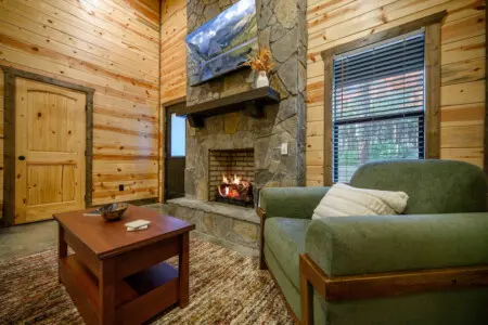 This cozy cabin living room has everything dialed in—a crackling stone fireplace, those super comfortable green chairs, and enough natural wood around you to remind you that you're genuinely disconnected from the rest of the world.