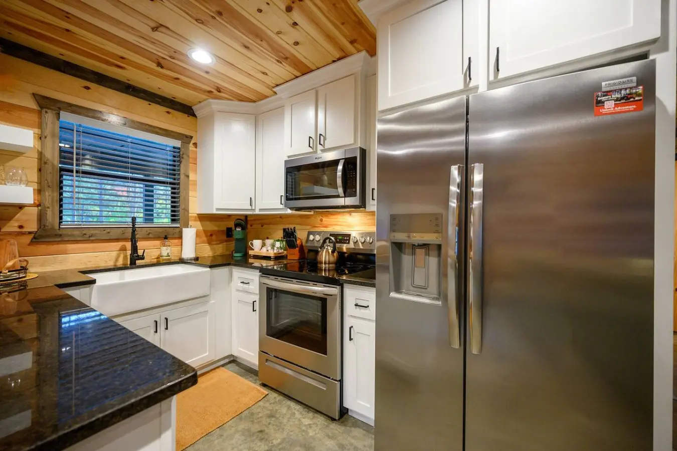 This kitchen is basically the dream setup for a getaway—stainless steel appliances, crisp white cabinetry, dark countertops, and that beautiful wood ceiling overhead making everything feel both modern and cozy at the same time.