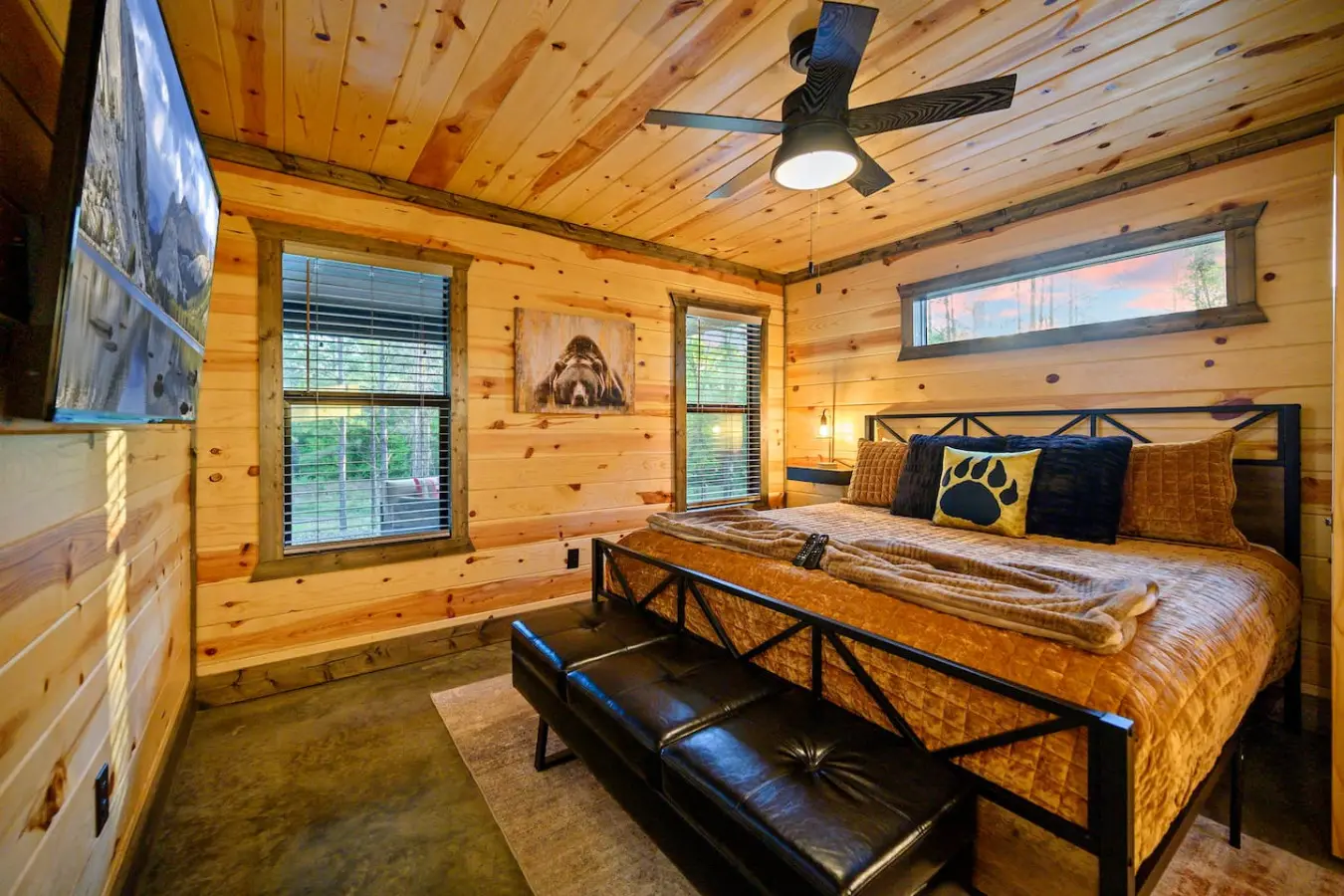 This bedroom totally nails that cozy cabin feel with warm wood everywhere, a killer bed setup, those big windows bringing the forest right in, and a ceiling fan keeping things comfortable.