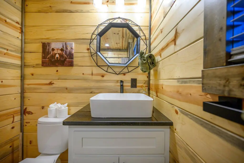 This bathroom hits the perfect balance between rustic cabin charm and modern updates, with those warm wood walls framing a sleek white vessel sink that honestly looks like something you'd see in a fancy spa.