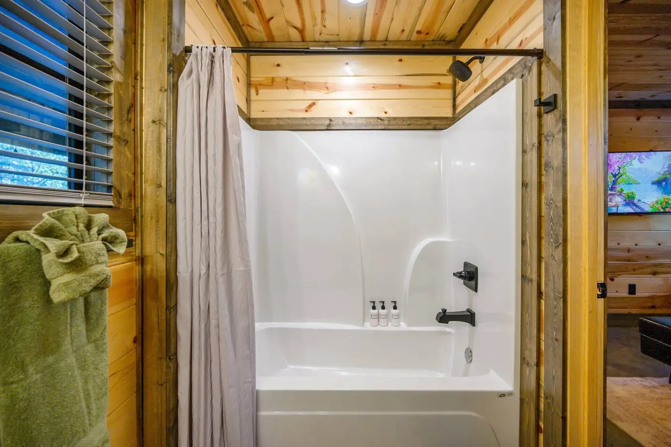 The shower setup here is all you need for a relaxing rinse after a day in the woods—clean white surround, quality fixtures, and those cozy wood beams overhead keeping it feeling like a true cabin escape.