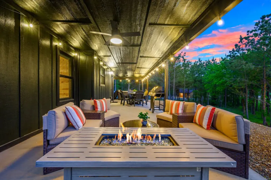 This covered patio is basically the ultimate hangout spot—fire pit in the middle, comfy seating all around, and those forest views at sunset are absolutely unreal.