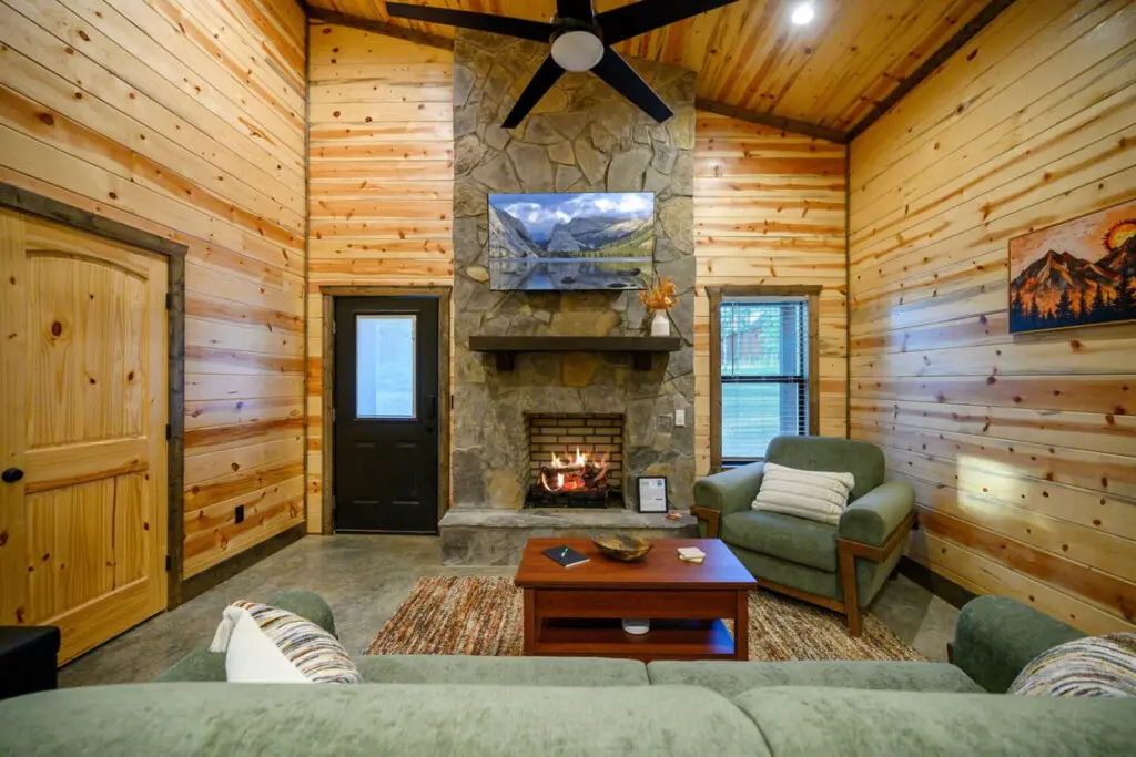 This cozy log cabin living room has all the vibes—a stone fireplace, comfy seating, and a view of the mountains right on the TV to match the real ones outside your window.