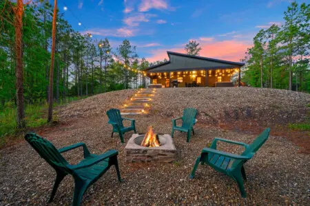 There's something magical about gathering around a fire pit surrounded by towering pines as your modern retreat glows warmly against the twilight sky.