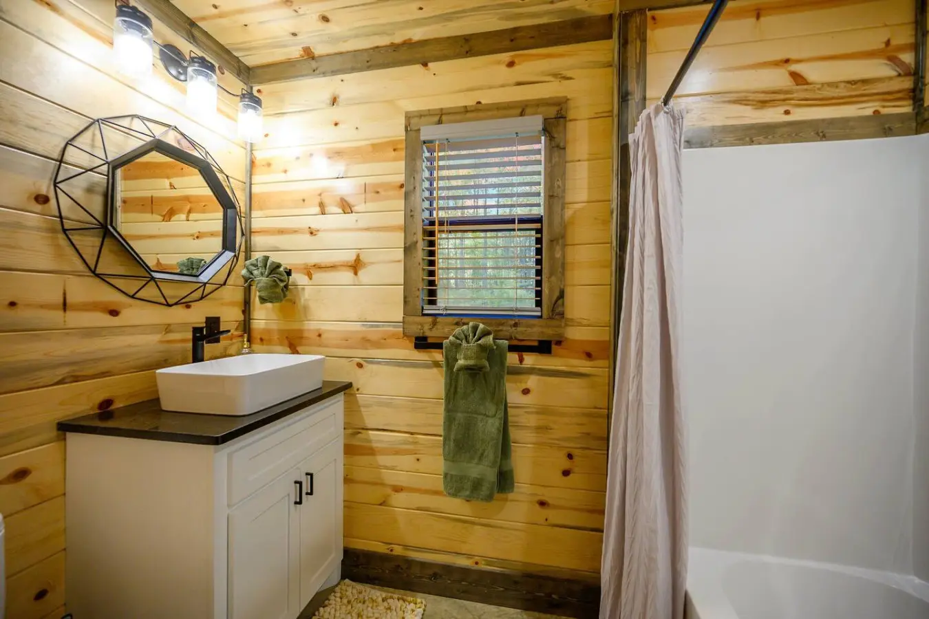 This rustic cabin bathroom is honestly goals—all that warm knotty pine, a sleek modern sink, natural light pouring in, and a rainfall showerhead that's definitely going to make your morning routine feel like a spa day.