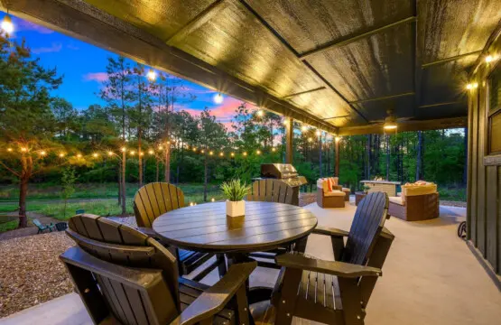 This covered patio setup is giving major entertaining energy with that spacious dining table, lounge seating, and a built-in grill all wrapped up under warm lighting while the forest melts into that gorgeous twilight sky.