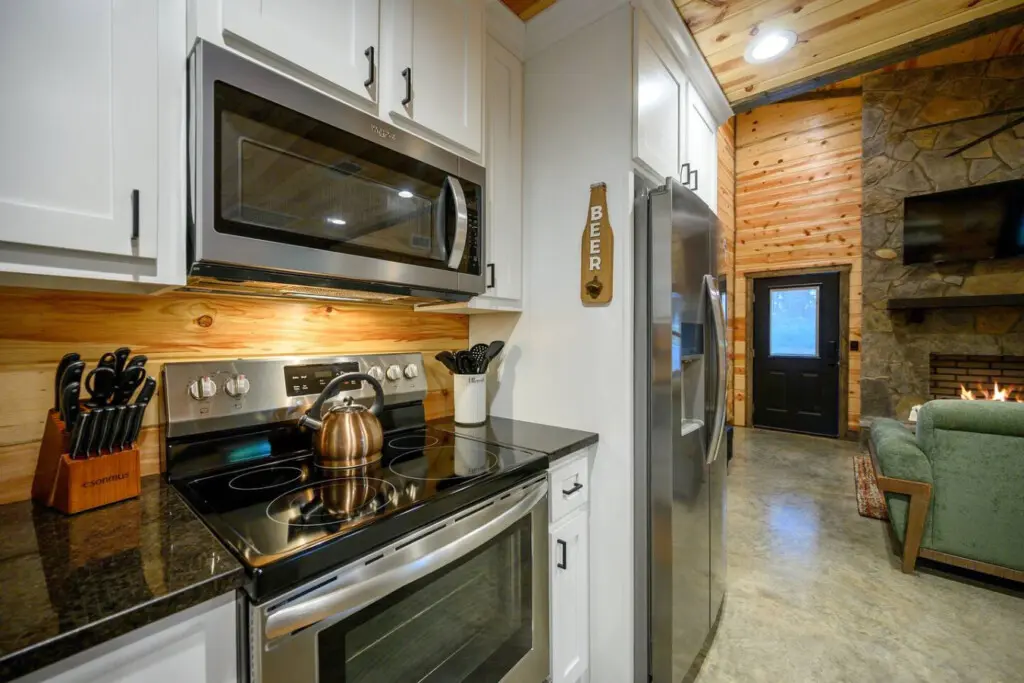 This kitchen perfectly blends modern updates with cozy cabin vibes—crisp white cabinetry, stainless steel appliances, and that gorgeous warm wood backsplash that ties everything together.