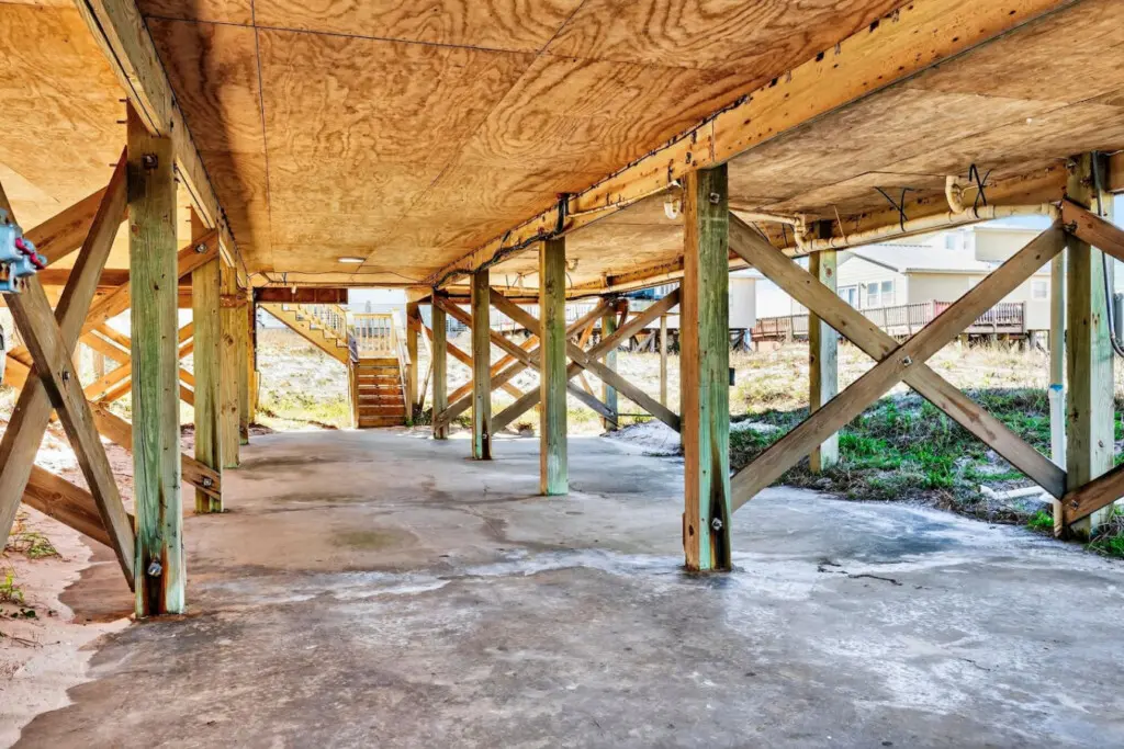 Beneath the soaring ceilings and weathered beams, this sheltered under-home space is your private transition zone between cozy indoors and endless sandy shores—complete with direct beach access and that perfect coastal breeze flowing through.