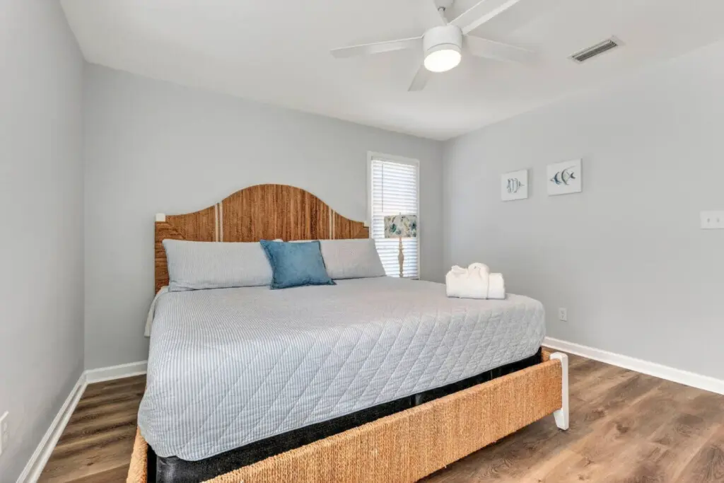 Wake up in this peaceful coastal bedroom with a warm wood headboard, crisp linens, and a ceiling fan keeping the ocean breeze flowing all day long.
