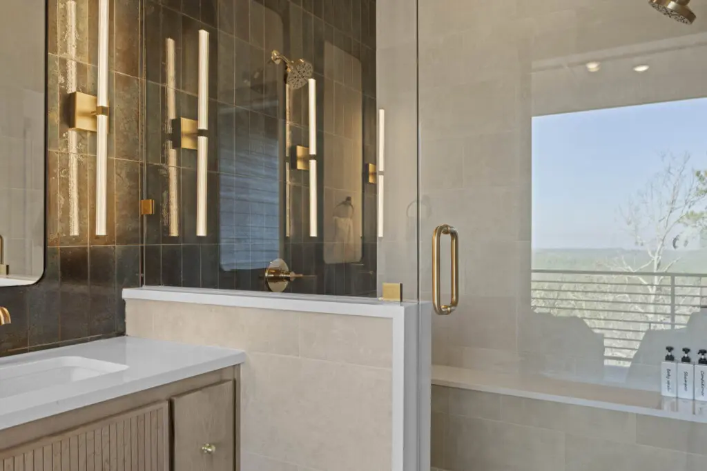 The master bath has that moody dark tile, brass fixtures, and a shower view that looks out over the treetops.