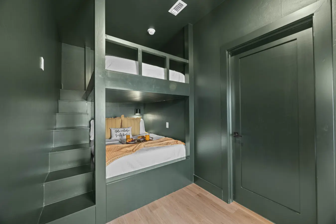 The kids (or let's be honest, adults) get this moody green bunk setup with built-in stairs and cozy reading lights.