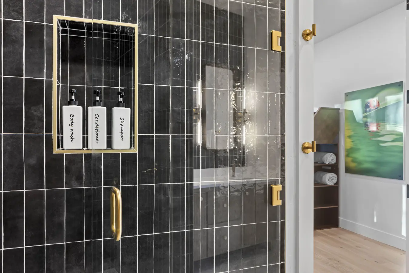 The shower's got that moody black tile with gold hardware and labeled dispensers so no one's guessing which bottle is shampoo.