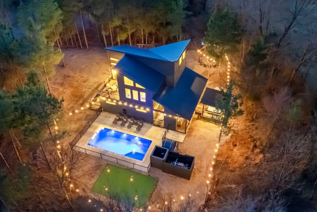 This stunning modern cabin sits tucked in the woods with a glowing pool and string lights creating the perfect cozy forest getaway vibe.