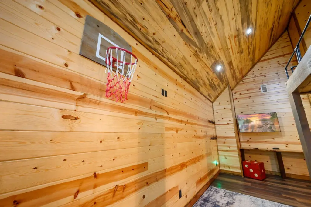 This cozy game room features wood walls, a basketball hoop, and plenty of space for indoor fun.