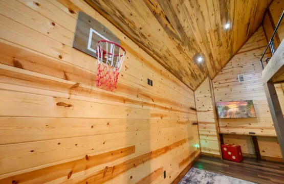 This cozy game room features wood walls, a basketball hoop, and plenty of space for indoor fun.