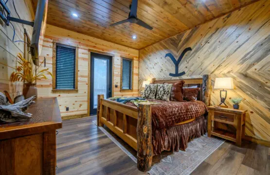 This cozy log cabin bedroom features rustic wood finishes, a sturdy timber bed, and plenty of natural light from multiple windows.
