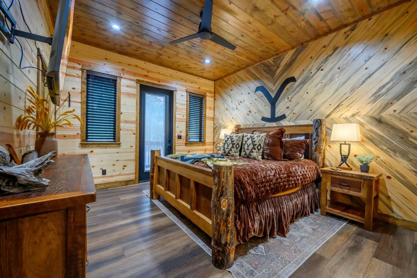 This cozy log cabin bedroom features rustic wood finishes, a sturdy timber bed, and plenty of natural light from multiple windows.