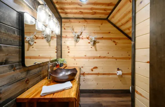 This rustic log cabin bathroom features a stunning vessel sink and exposed wood beams with antler décor throughout.