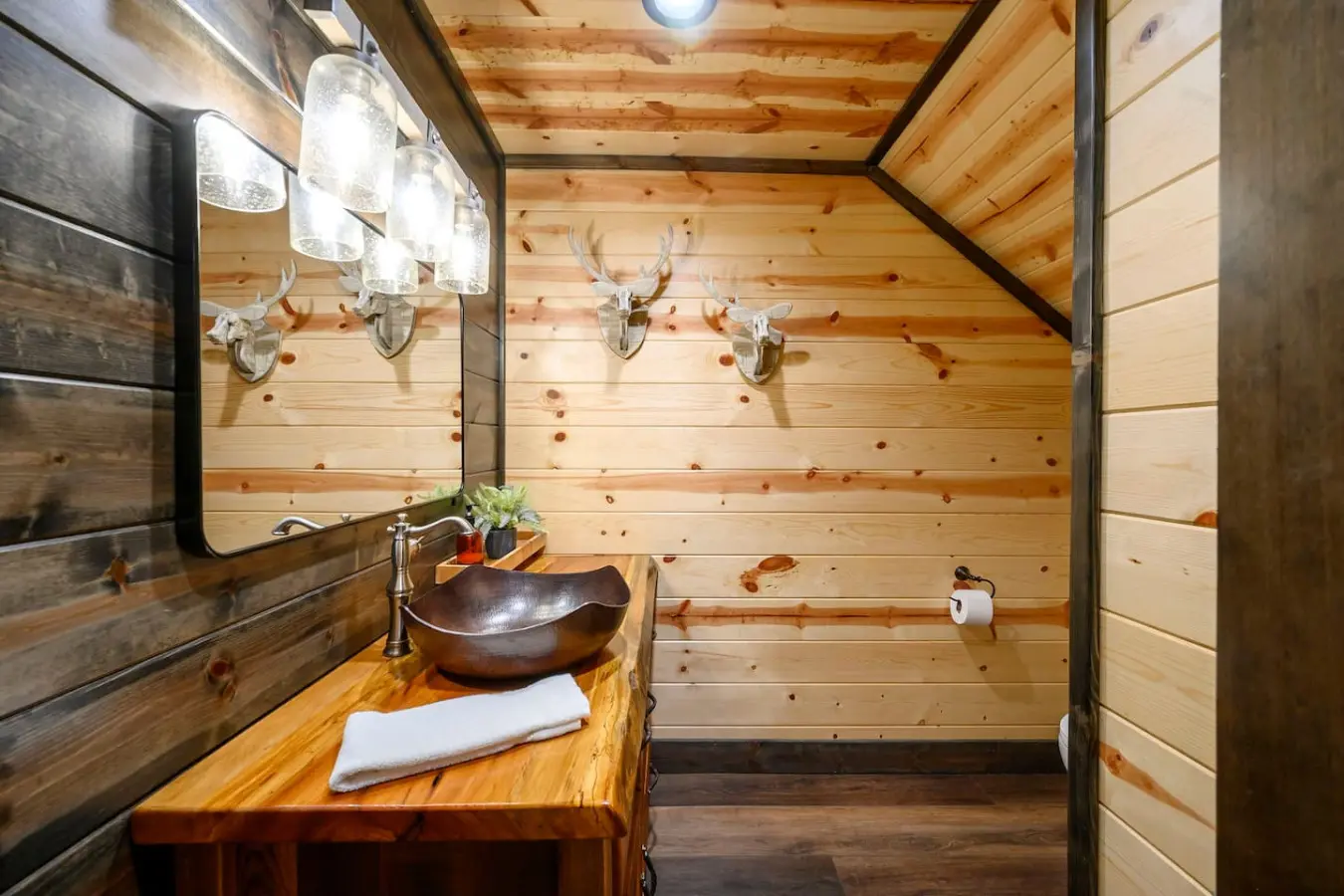 This rustic log cabin bathroom features a stunning vessel sink and exposed wood beams with antler décor throughout.
