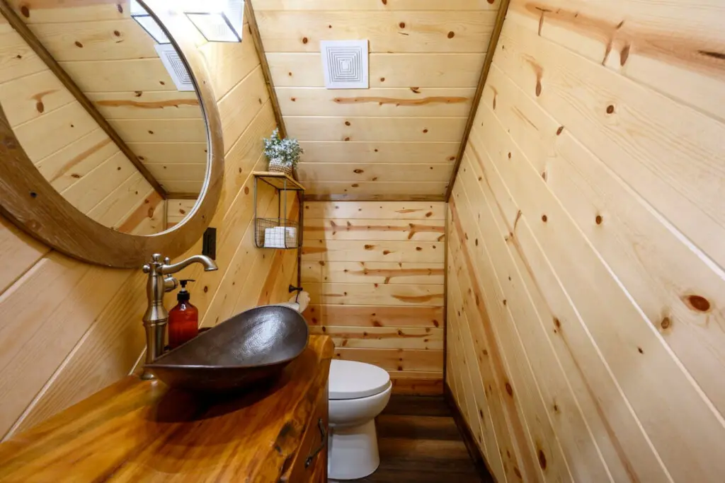 This cozy wood-lined bathroom in our tiny home features a stunning handcrafted sink and all the essentials you need.