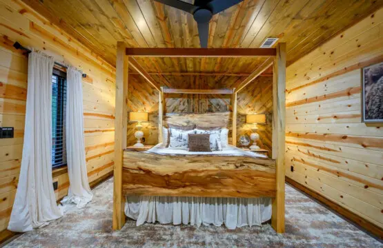 This log cabin bedroom features a stunning custom four-poster bed with vaulted wood ceilings and cozy mountain views.