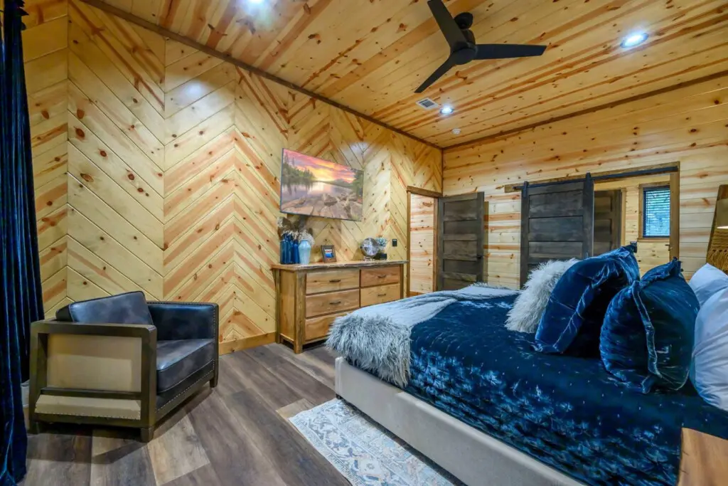 This stunning log cabin bedroom features luxe bedding, a cozy reading nook, and beautiful herringbone wood walls throughout.
