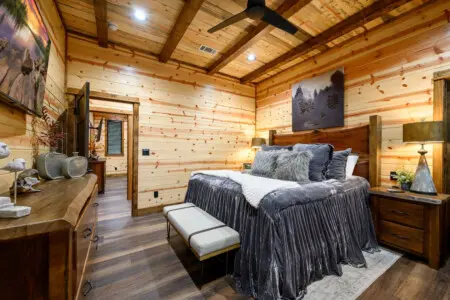 This cozy log cabin bedroom features a rustic wooden bed, warm knotty pine walls, and modern amenities perfect for a peaceful retreat.