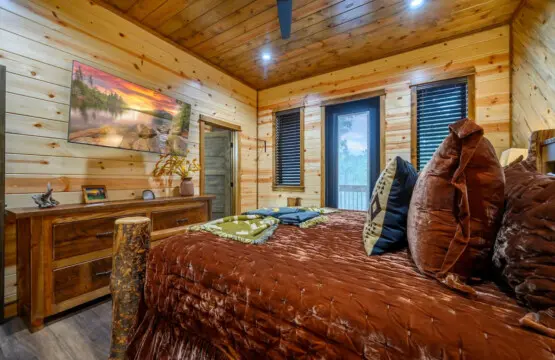 This cozy log cabin bedroom features warm wood throughout, a king bed, and those big windows bringing in tons of natural light.