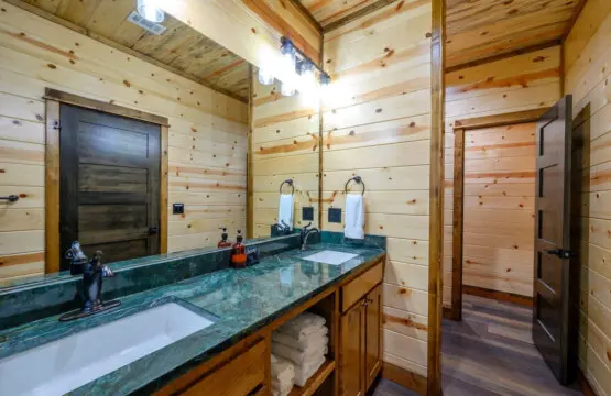 This spacious log cabin bathroom features a stunning dual vanity with green marble countertops and custom wood finishes throughout.