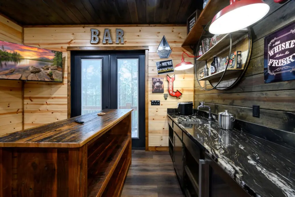 This custom bar space features rustic wood finishes, sleek black countertops, and direct access to the outdoor deck.