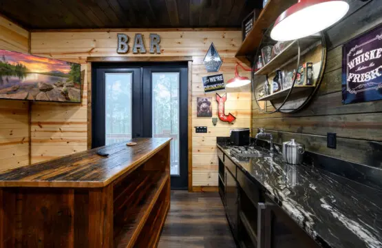 This custom bar space features rustic wood finishes, sleek black countertops, and direct access to the outdoor deck.