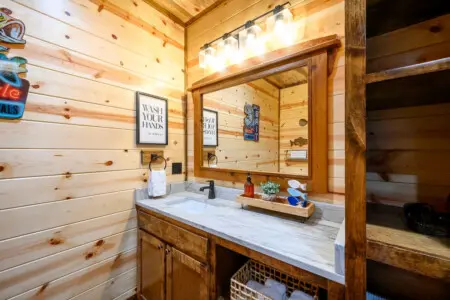 This cozy cabin bathroom features a spacious vanity with marble countertop and large mirror framed in natural wood.