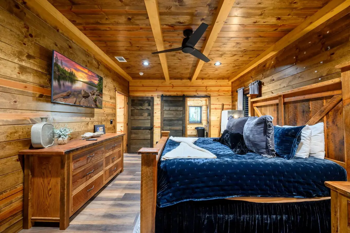 This cozy log bedroom features a king bed, rustic wood beams, and a flat-screen TV in a peaceful retreat setting.