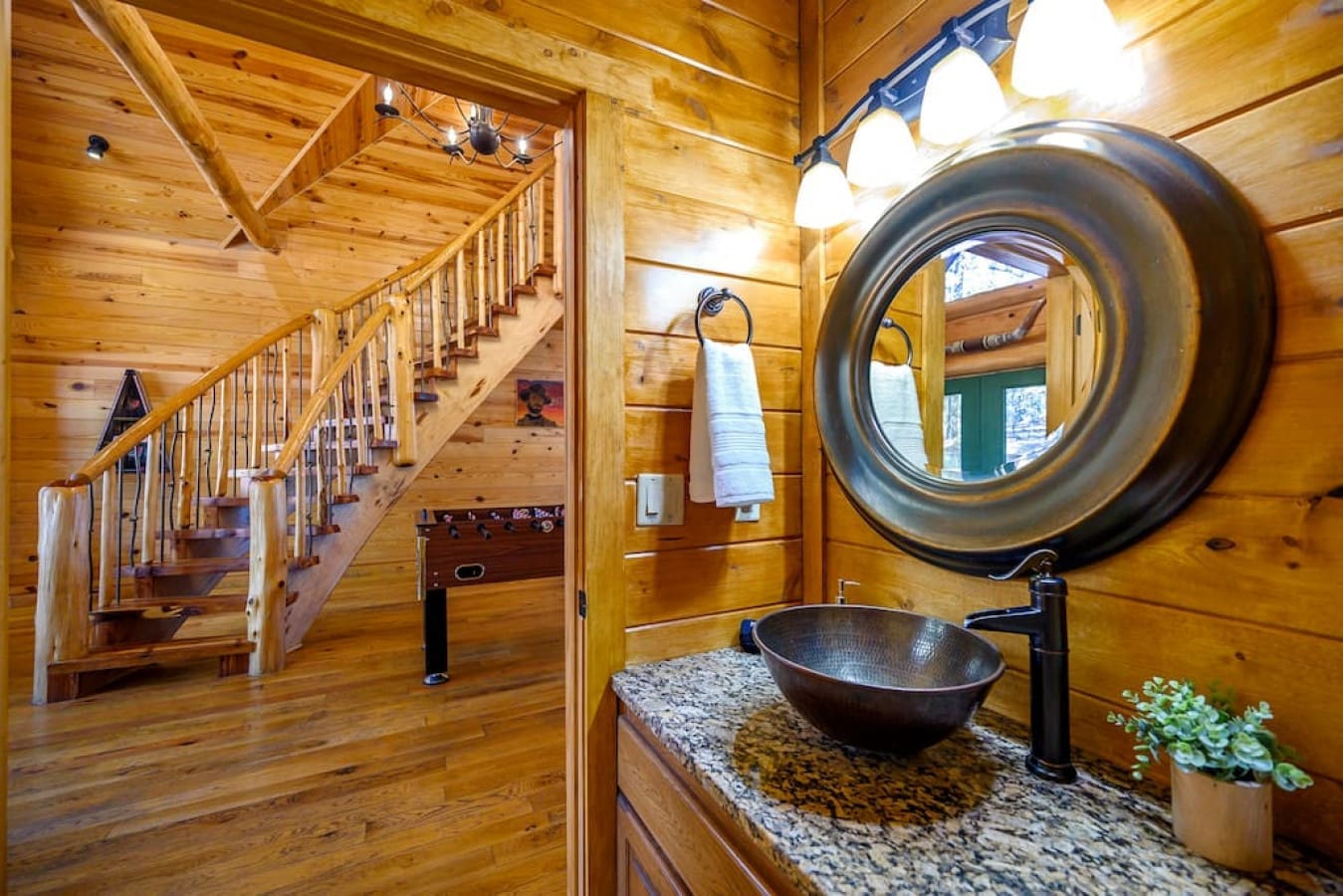Our elegant wooden stairs and a bathroom oasis featuring a stylish basin sink and faucet, illuminated by a mirror with lights at the top.