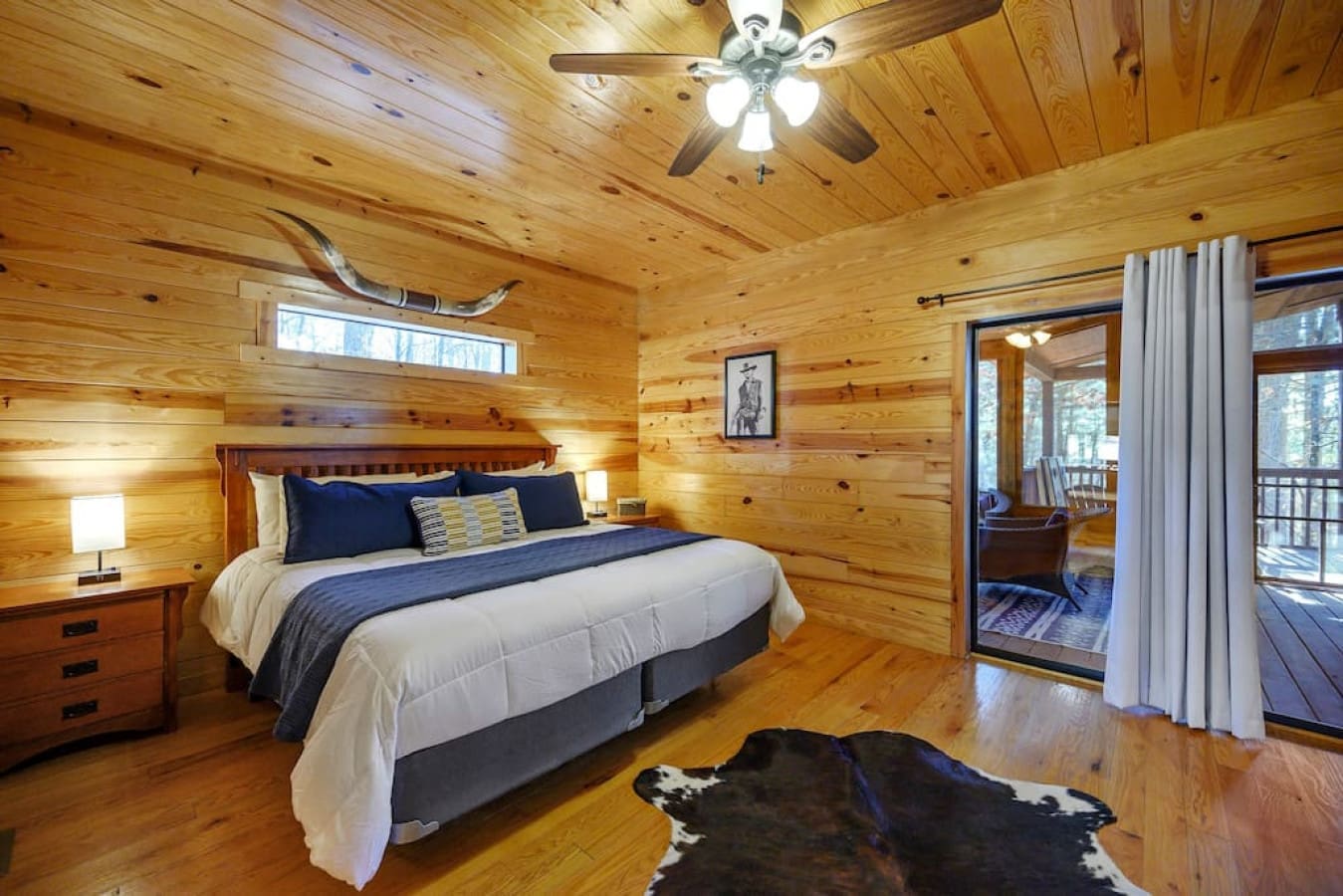 Our cabin's master bedroom features a comfortable king-sized bed and a view into the sunroom. This bright and welcoming space is a perfect spot to spend some time.