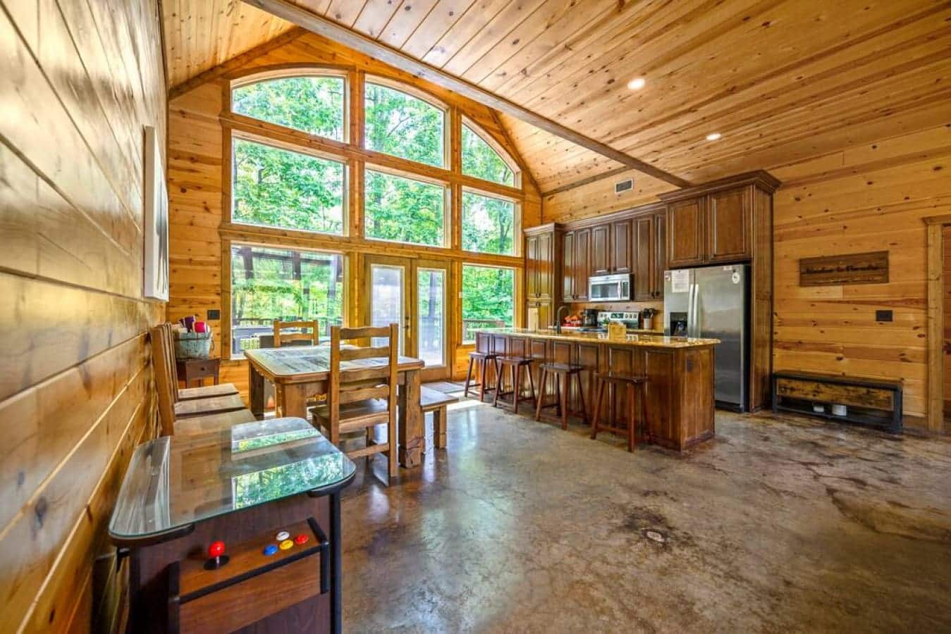 Bask in the warmth of the fireplace's glow as sunlight streams through the high windows, casting a cozy spell on this cabin's inviting open kitchen.