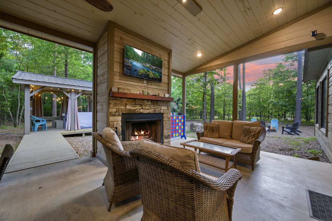 Large covered patio featuring a stone fireplace and comfortable wicker furniture.