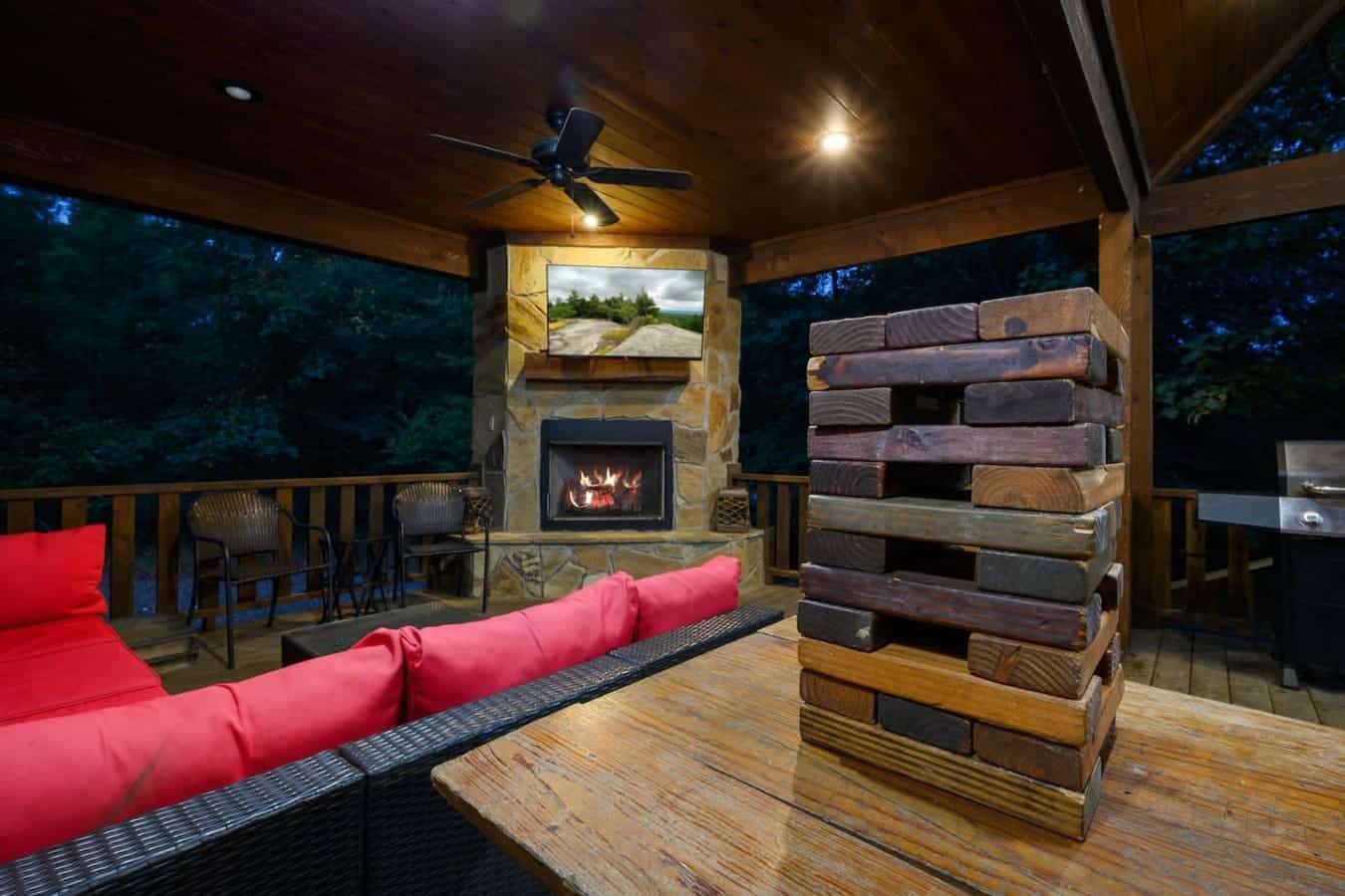 This covered deck is basically an outdoor living room with a fireplace, TV, and those massive stacked timber logs that somehow make the whole space feel like a giant rustic sculpture.