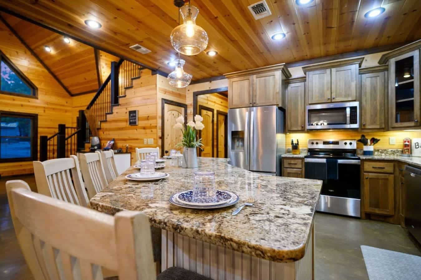 This granite island is basically command central for your whole crew—enough seating for everyone, stainless steel appliances, and that wood ceiling overhead making the whole kitchen feel like the heart of the cabin.