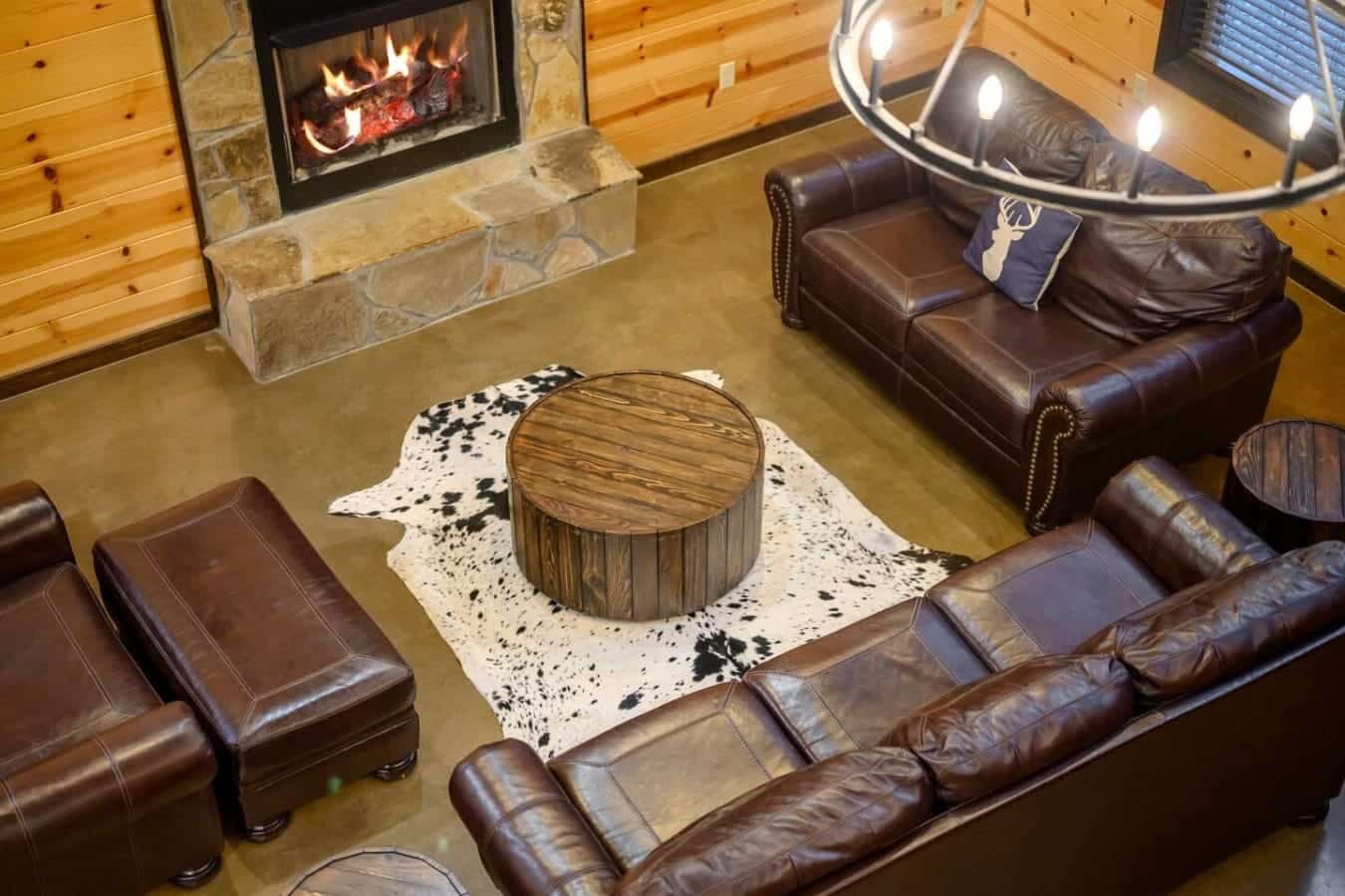 Gather around this barrel coffee table on that cozy cowhide rug while the fireplace glows behind you and leather seating wraps the whole crew in that perfect rustic comfort.