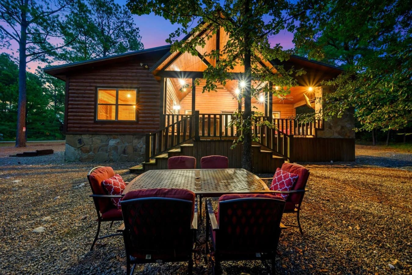 Twilight hits different when you're sitting around this outdoor table with the whole cabin lit up behind you and the forest going quiet all around.
