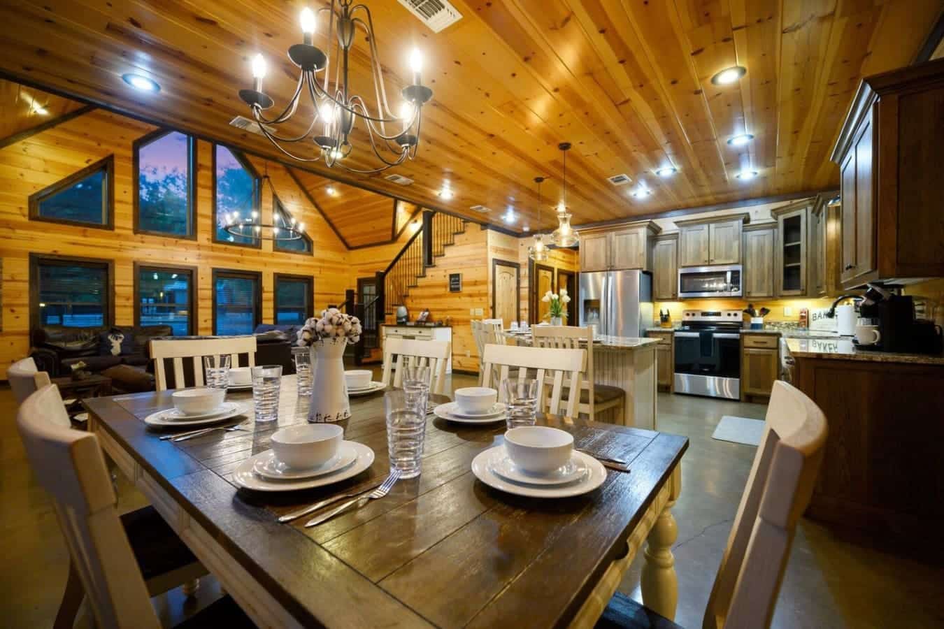 This dining table set for a feast, with those white-slat chairs and a flower centerpiece, sits right in the heart of this open-concept space where the vaulted wood ceilings, kitchen, and living area all flow together like one big invitation to settle in a